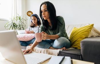 Lady holding cup sitting in couch while scrolling on laptop